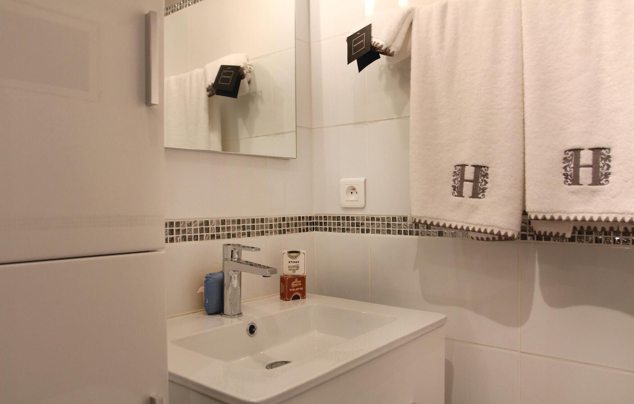 A bathroom with a white sink, a mirror, and two towels with a monogram.