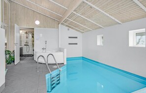 An indoor swimming pool with a blue interior, a white bathtub, and a wooden ceiling.