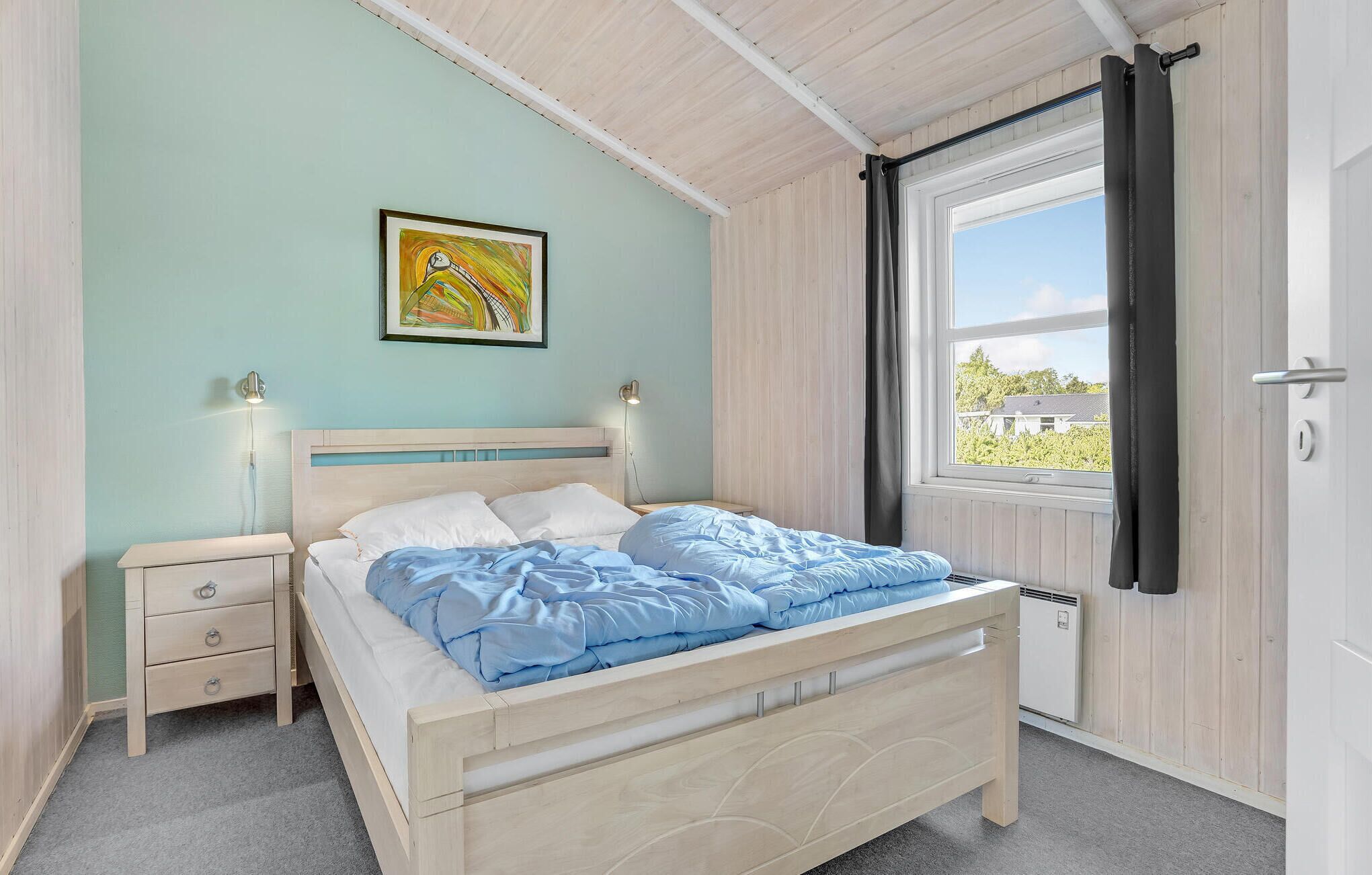 Une chambre à coucher avec un lit, des tables de chevet, une fenêtre avec des rideaux, un radiateur et un tableau au mur.
