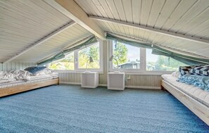 A cozy attic bedroom with two beds, large windows, and a sloped ceiling.