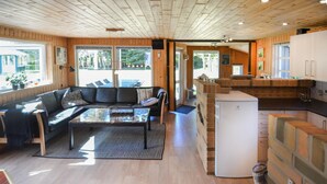 A cozy cabin interior with a living area featuring a sofa and a glass-top coffee table, a kitchen with a brick backsplash, and a refrigerator. - Gorgeous home in Spøttrup (Spøttrup)