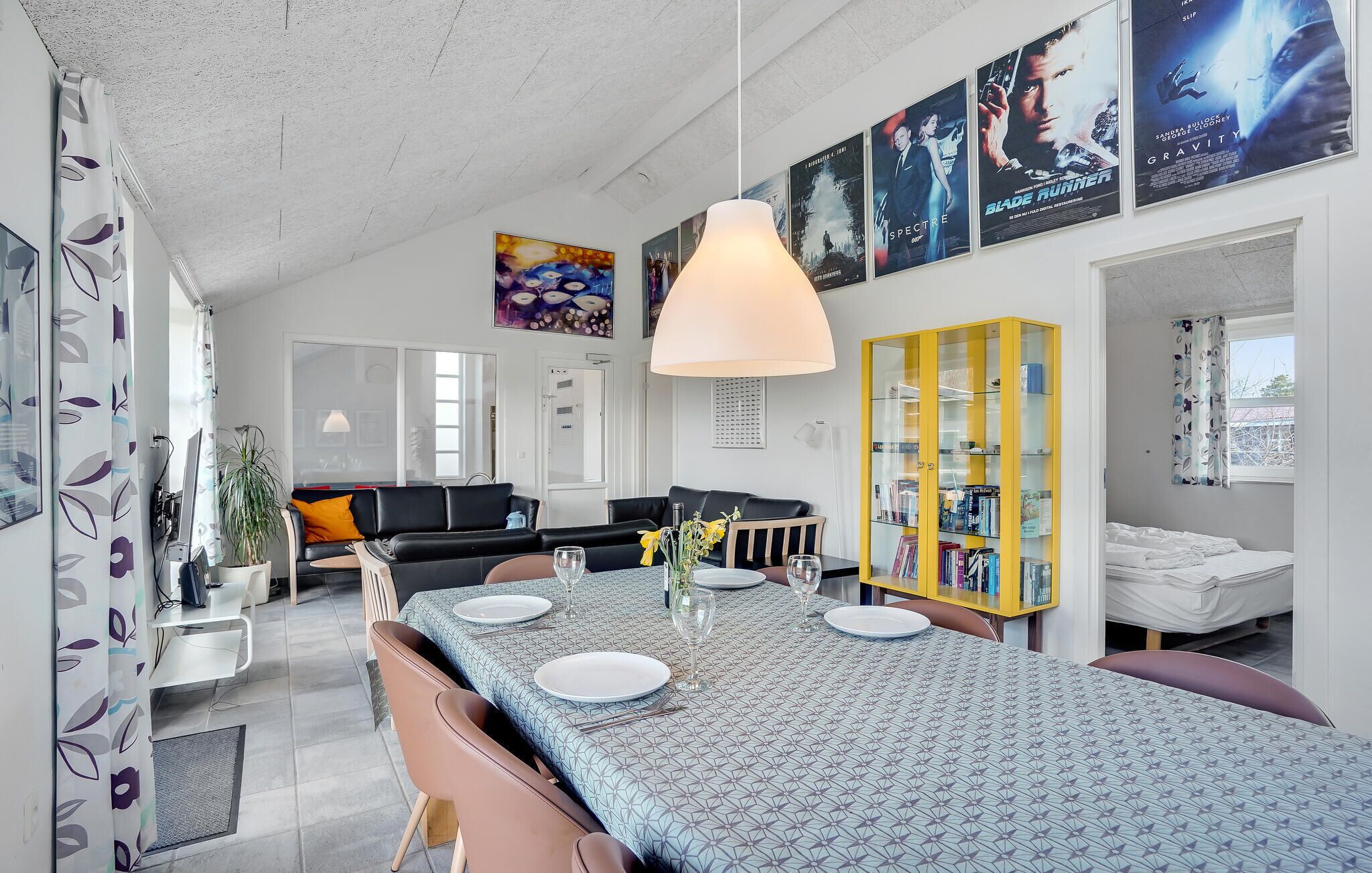 Ein modernes Wohnzimmer mit Essbereich, einem gelben Bücherregal und Filmplakaten an der Wand.
