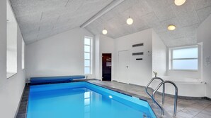 A swimming pool with a blue interior, a white ceiling, and a window providing natural light. - Amazing home in Oksbøl with sauna (Oksbøl)