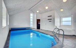 Een zwembad met een blauw betegeld interieur, een wit plafond en een raam dat natuurlijk licht binnenlaat.
