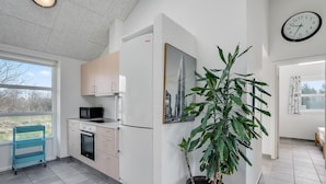 A modern kitchen with a microwave, oven, and refrigerator, a large potted plant, and a cityscape painting. - Amazing home in Oksbøl with sauna (Oksbøl)