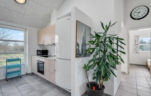 A modern kitchen with a microwave, oven, and refrigerator, a large potted plant, and a cityscape painting. - Amazing home in Oksbøl with sauna (Oksbøl)