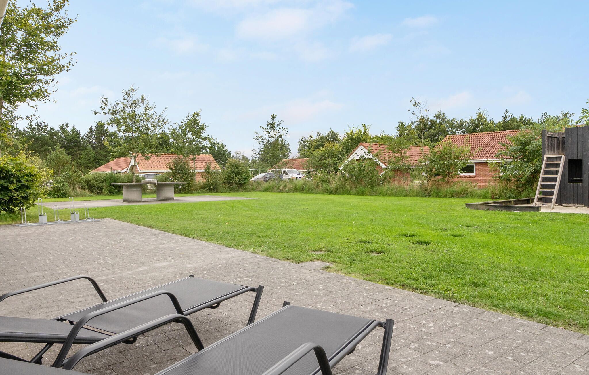 Ein Terrassenbereich im Freien mit einem gepflasterten Weg, Metallstühlen und einem Rasen.