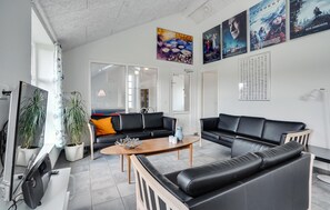 A modern living room with black leather sofas, a wooden coffee table, and a TV. There are potted plants and a poster on the wall. - Amazing home in Oksbøl with sauna (Oksbøl)