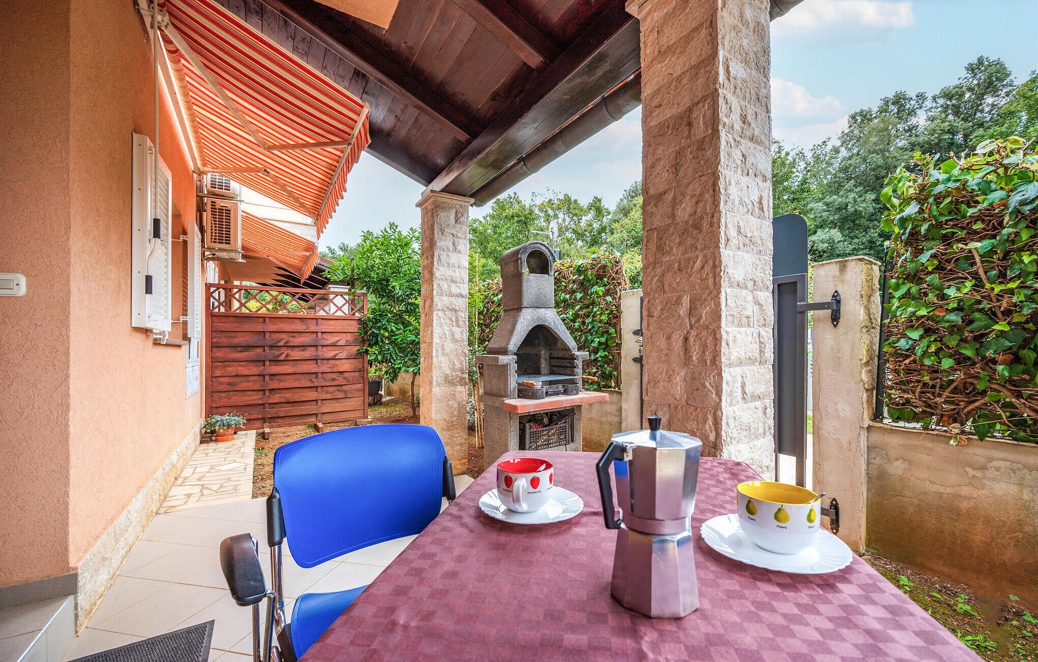 Eine Terrassenanlage im Freien mit einem Tisch für zwei Personen, einem Steinofen und einem Holzzaun.