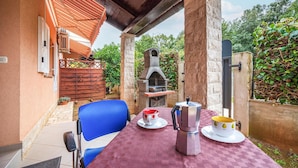 An outdoor patio with a table set for two, a stone oven, and a wooden fence. - Stunning apartment in Pula with WiFi (Pula)