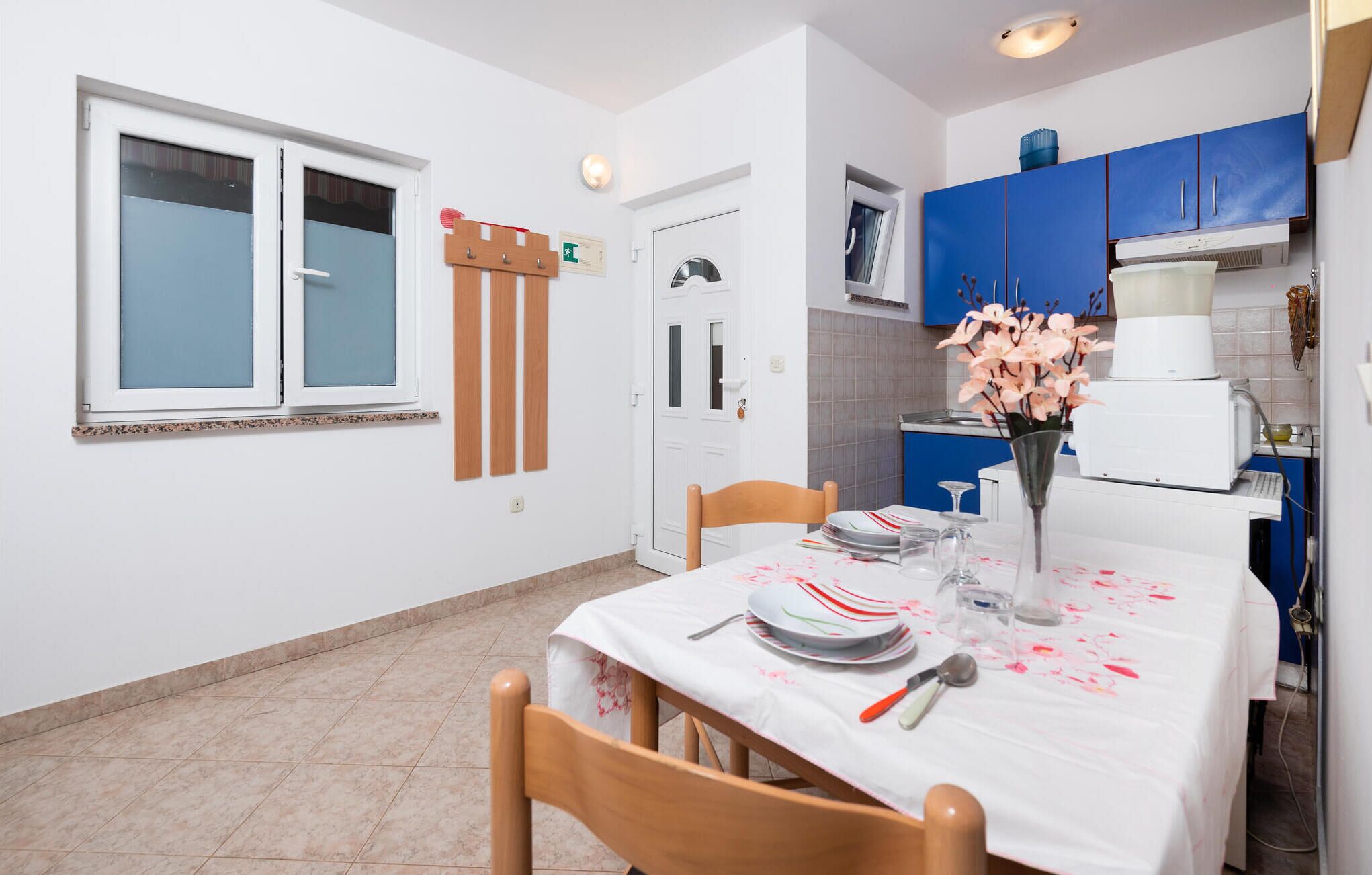 A small kitchen with blue cabinets, a white refrigerator, and a dining table set with plates and a vase of flowers.