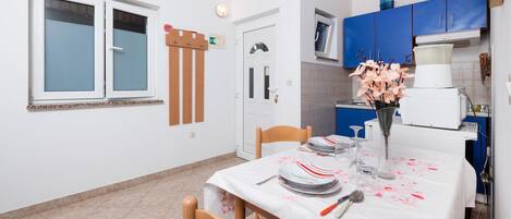 A small kitchen with blue cabinets, a white refrigerator, and a dining table set with plates and a vase of flowers.