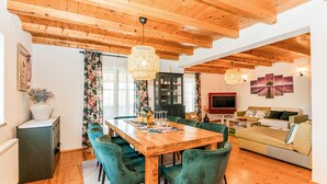 A dining area with a wooden table and green upholstered chairs, a living room with a sofa and TV, and a kitchen with a cabinet. - Beautiful home in Prolozac Donji (Prolozac Donji)