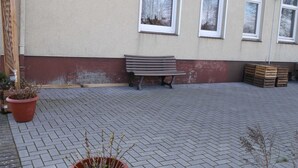 Zona exterior pavimentada amb una banca, plantes en testos i caixes de fusta.