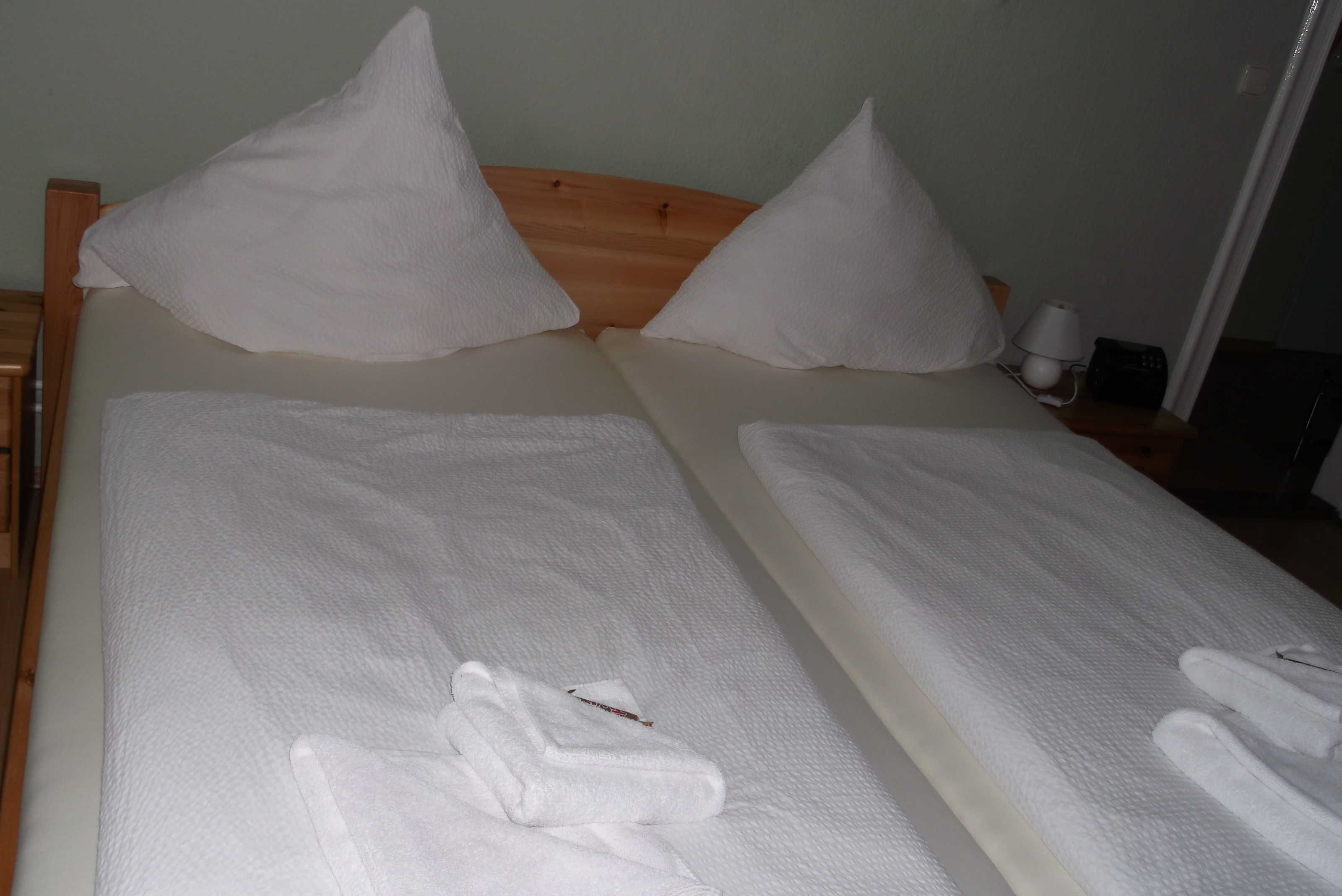 Ein Doppelbett mit weißen Bettwäsche und Kissen, ein Holz-Kopfstück und ein Nachttisch mit Lampe und Telefon.
