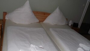 Un llit doble amb llençols i almoades blanques, un panell frontal de fusta i una taula de nit amb una làmpada i un telèfon.