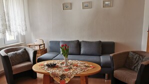 Un saló amb un sofà blau, dues butaques, una taula de centre de fusta amb un corredor floral, i un ram de flors vermelles.