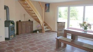A spacious room with a wooden staircase, a fireplace, and a large window offering a view of the outdoors. - Apartment 1 - Rügen apartment 119 (Garz/Rügen)