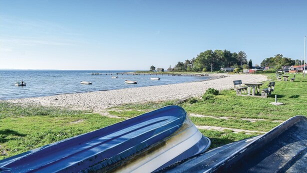 Una platja amb vaixells, un tram de sorra i cases al fons.