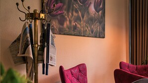 Una habitación con una araña, un atril de periódicos en la pared y un cuadro grande con motivos florales.