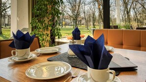 Una mesa de comedor dispuesta con platos, tazas y servilletas, con vista a árboles y un césped al exterior.