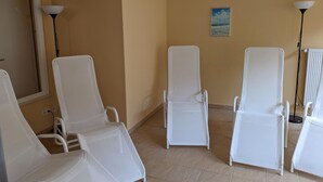 Une pièce comprenant quatre fauteuils blancs disposés en rangée, une grande fenêtre offrant une vue dégagée et un tableau accroché au mur.