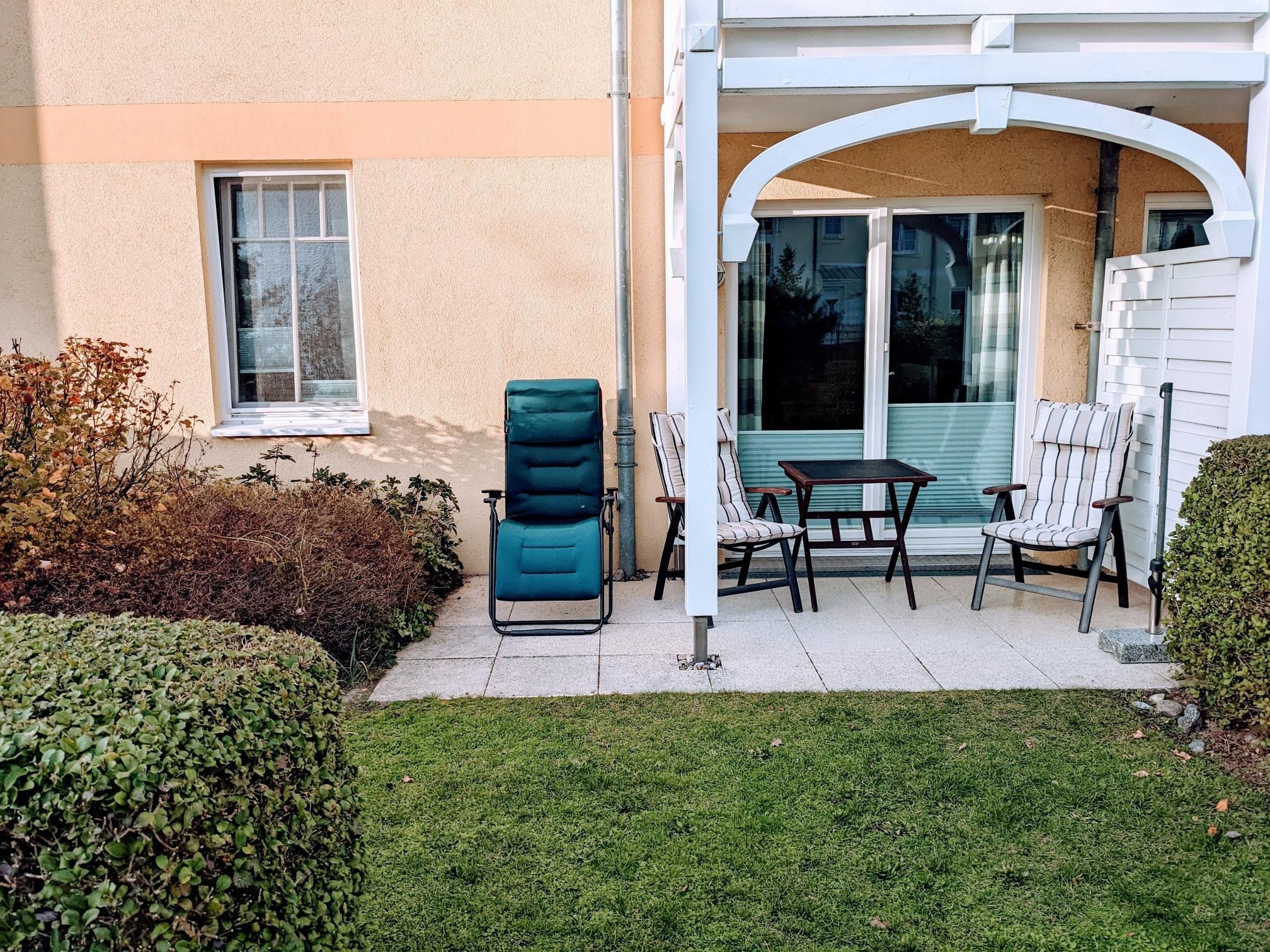 Un patio con una silla azul, dos sillas a rayas y una mesa.