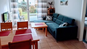 Un salon comprenant un canapé, une table à manger avec des chaises, un téléviseur et une bibliothèque.