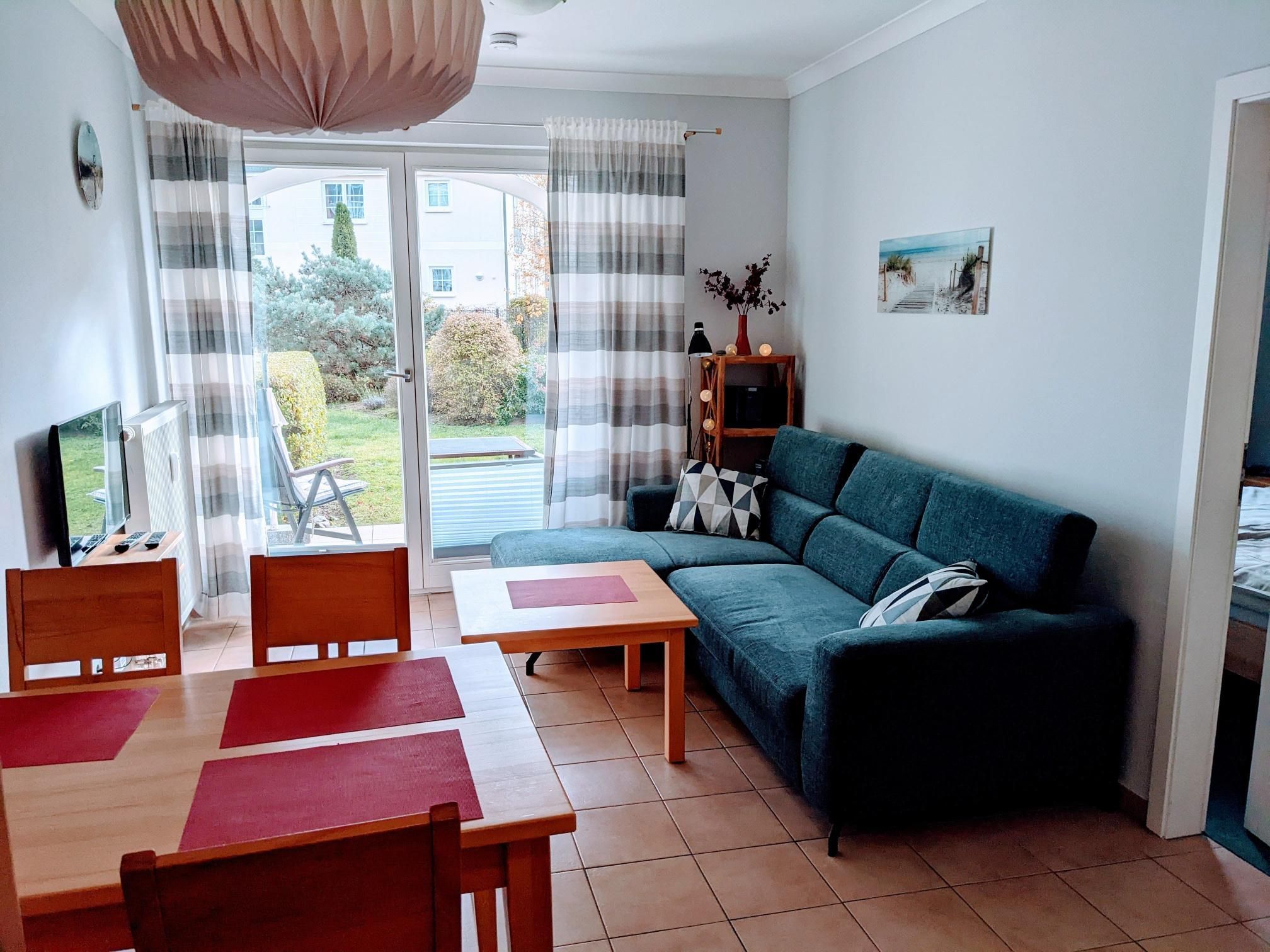 Ein Wohnzimmer mit einer Couch, einem Esstisch mit Stühlen, einem Fernseher und einem Bücherregal.