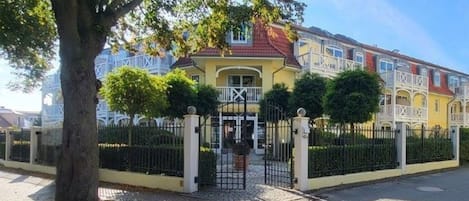 Un área residencial privada con reja, un edificio amarillo, un árbol y una cerca.