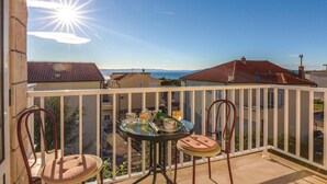 Un balcon avec une table et des chaises, donnant sur un quartier résidentiel aux toits recouverts de tuiles rouges et sous un ciel dégagé.