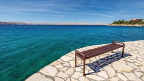 A bench on a stone platform by a clear blue sea with a distant shoreline. - 2 bedroom gorgeous apartment in Ribarica (Ribarica)