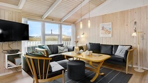 Ein gemütliches Wohnzimmer mit Holzboden, einem Flachbildfernseher, einer Couch, einem Couchtisch und einem Esstisch.