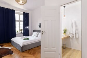 A bedroom with a bed, a window with curtains, a door leading to a bathroom, and a wooden floor.