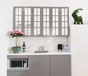 Una cocina moderna con armarios grises, encimera blanca, horno integrado, cafetera y una planta en maceta.