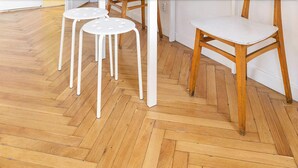 Un suelo de madera con estampado de espiga, una silla blanca y una mesa blanca.