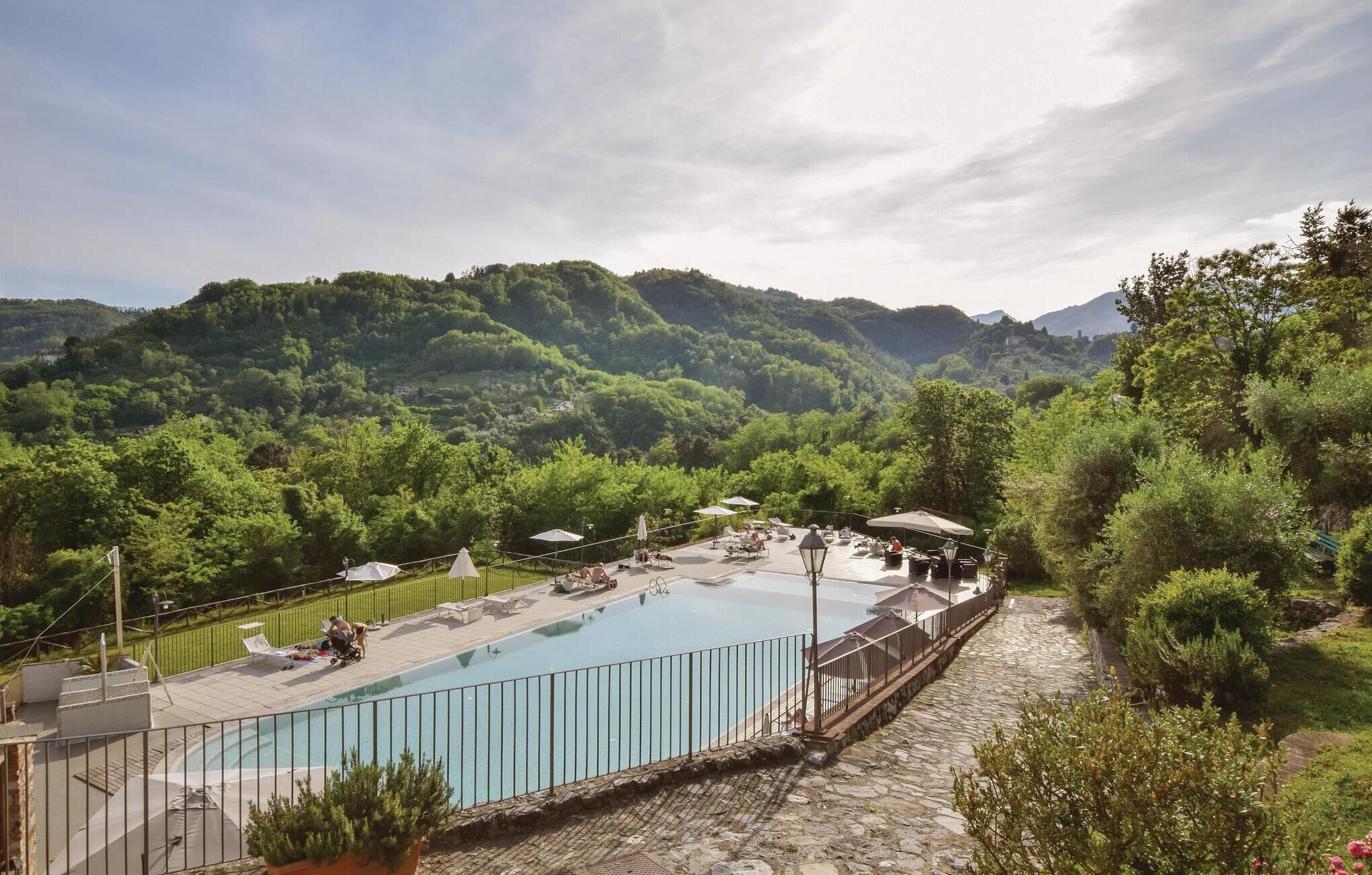 A swimming pool with lounge chairs and umbrellas, surrounded by lush greenery and mountains.