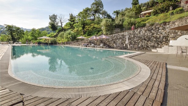 A large outdoor swimming pool with a wooden deck surrounding it, stone walls, and outdoor seating areas. - Awesome home in Borgo a Mozzano LU (Borgo a Mozzano LU)