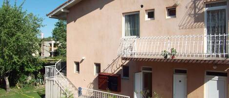 A two-story building with a balcony, a wooden fence, and a garden area.
