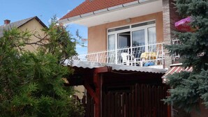 Una casa de dos pisos con techo de tejas rojas, un balcón con barandas blancas y una valla de madera en la parte delantera.