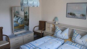 Een slaapkamer met een bed, een dressoir, een stoel, een spiegel en een hanglamp.