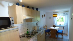Een kleine keuken met een magnetron, fornuis en spoelbak. Er is een eethoek met een tafel en stoelen.