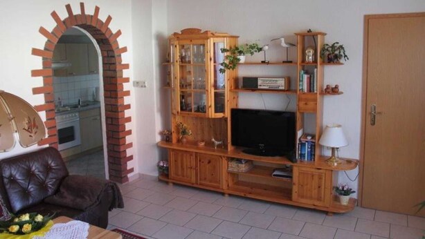 Een woonkamer met een bakstenen bogenboog, een houten entertainmentkast, een leren bank en een televisie.