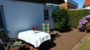 Een terras met een tafel, stoelen, een bloempot en een geplaveid pad.