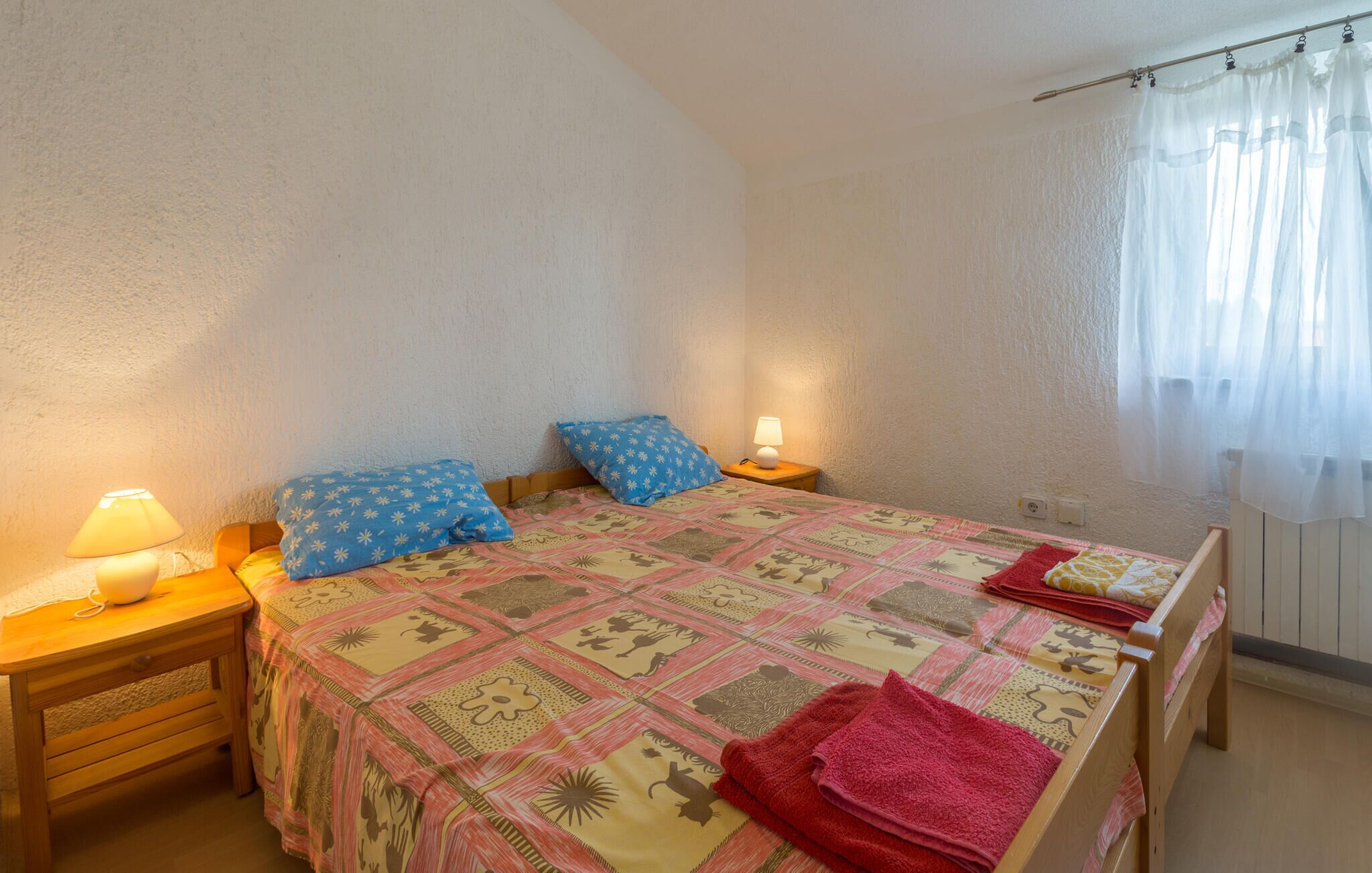A bedroom with a bed, two pillows, a nightstand with a lamp, and a window with curtains.