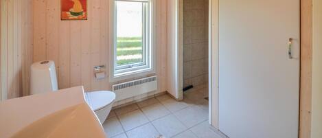 Un baño con paredes de madera, un inodoro, una ventana y una zona de ducha.