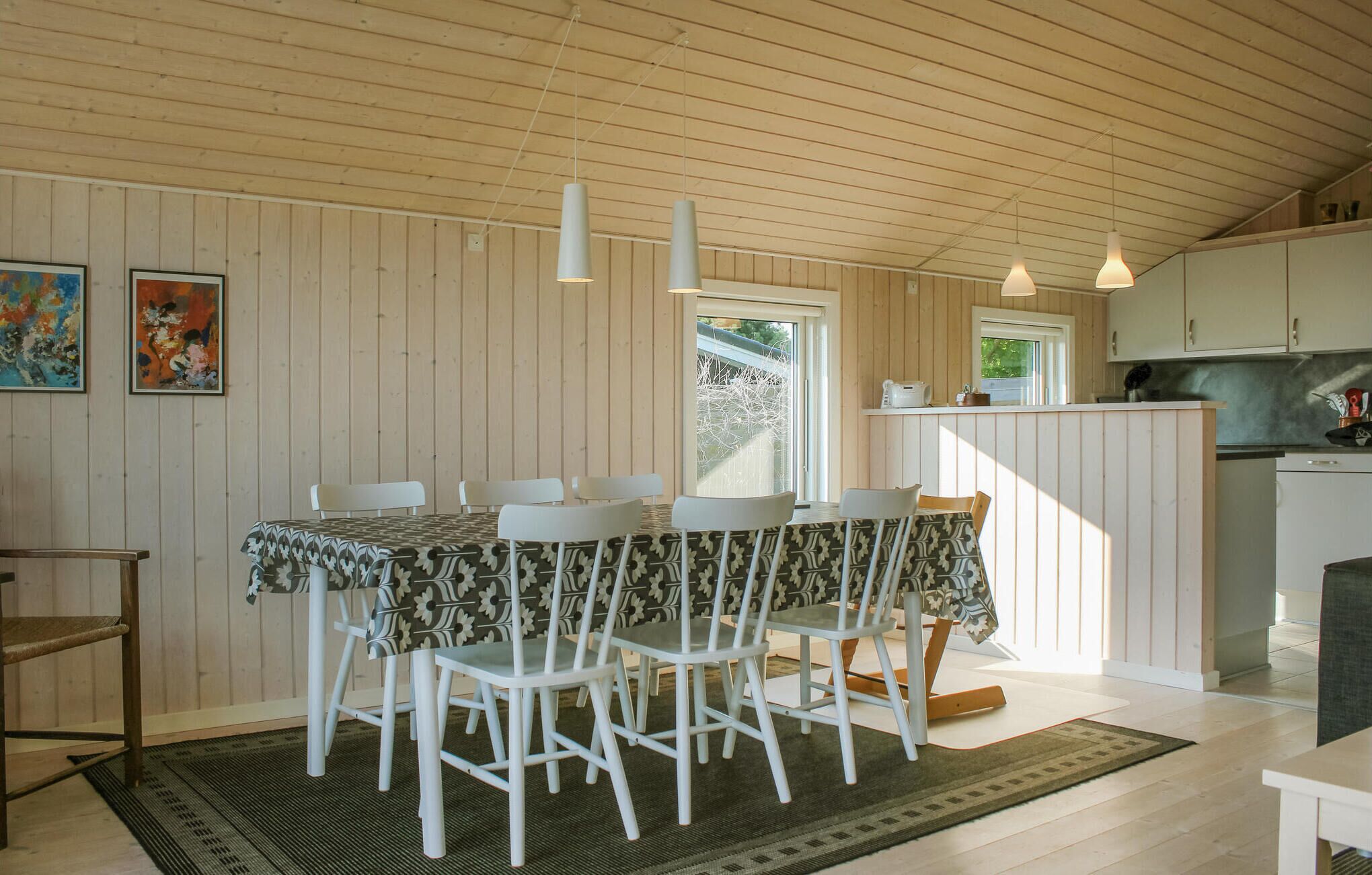 Un coin repas avec une table et des chaises en bois, une cuisine en arrière-plan et une fenêtre donnant sur un beau paysage.