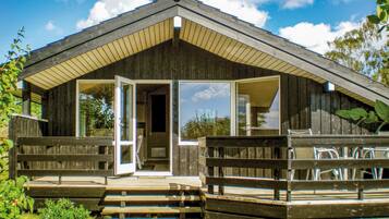 Une cabane en bois dotée d’une véranda, de grandes fenêtres et d’une porte donnant sur l’intérieur.