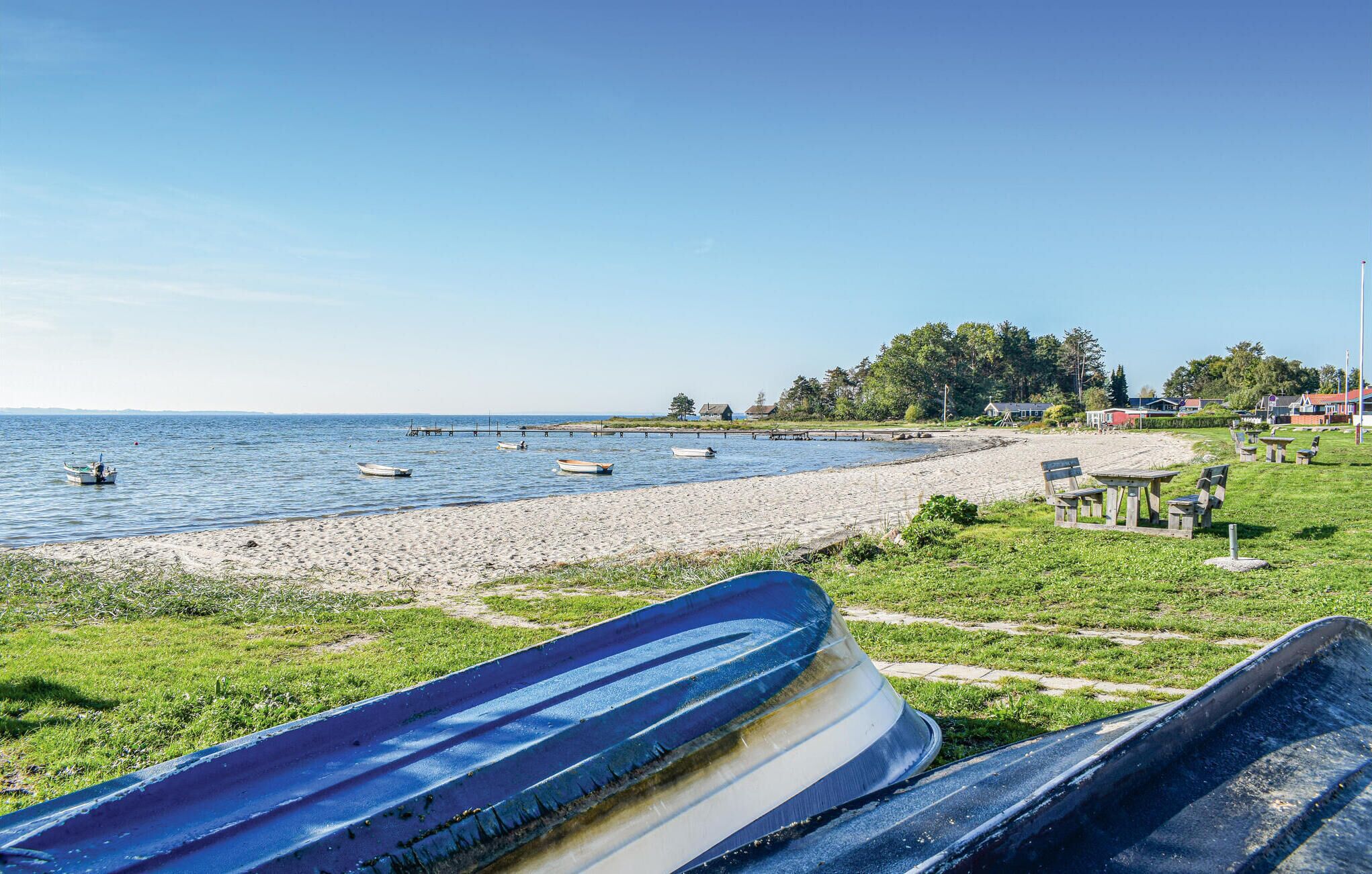 Une plage avec des bateaux, une jetée en bois et des maisons en arrière-plan.