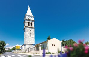 A stone tower with a pointed roof, a pedestrian crossing sign, and a building with a tiled roof.